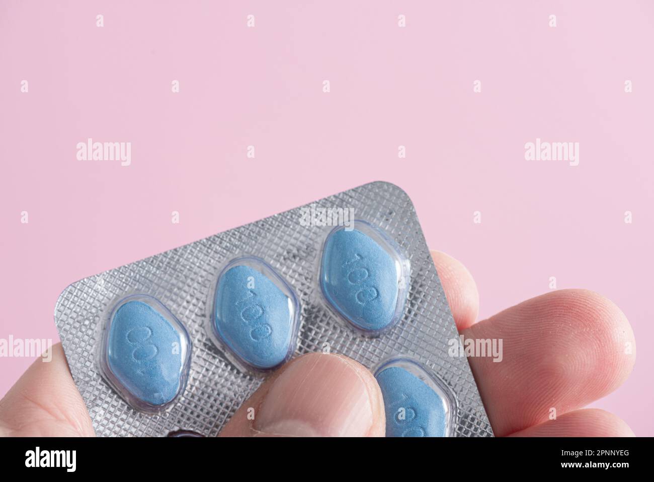 Man hold blue pill packaging on pink background. Medicine concept of medication for potency, erection, treatment of erectile dysfunction Close up Stock Photo