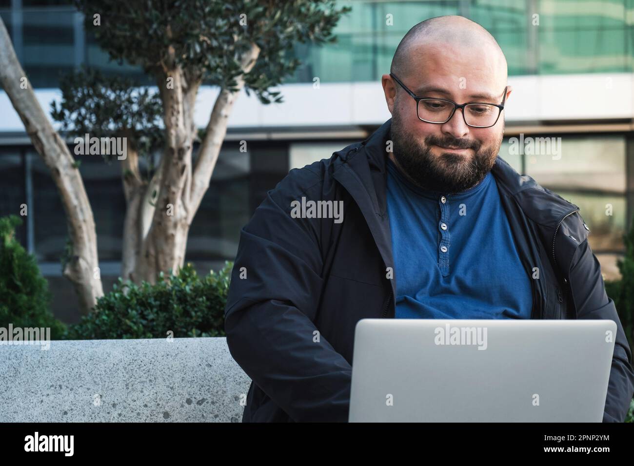 Plus size man in glasses using laptop while working outdoors. Male freelancer or IT specialist using computer for remote work Stock Photo