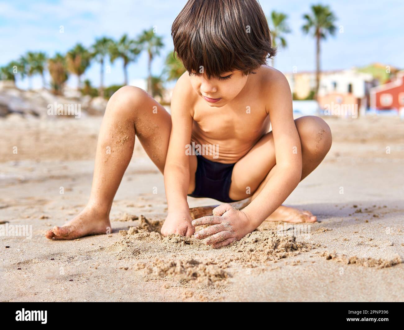 elementary age kid playing on the beach sand with palmtrees background Stock Photo