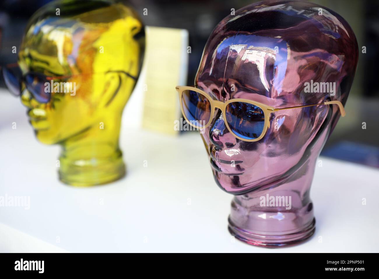 Two colorful glass female heads, tinted in purple and yellow, wearing glasses in an optician's window display Stock Photo