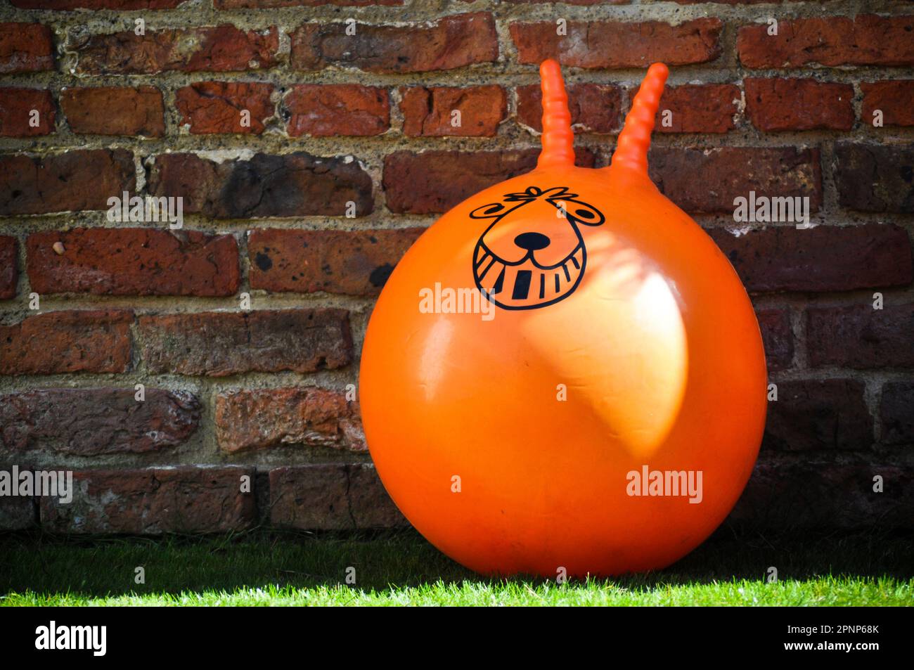 An orange space hopper toy propped against a rustic brick wall with copy space to the side Stock Photo