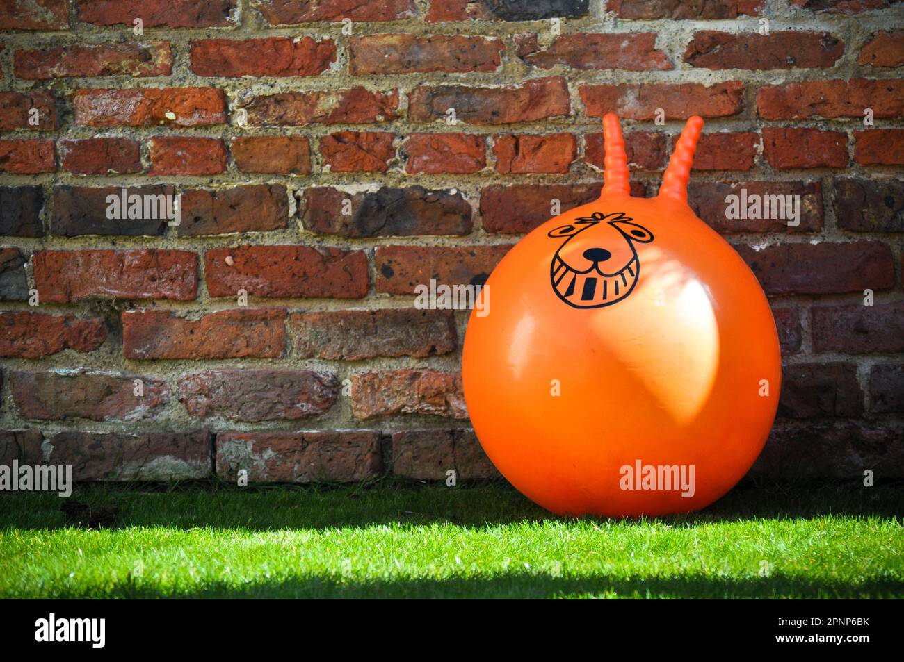 An orange space hopper toy propped against a rustic brick wall with copy space to the side Stock Photo