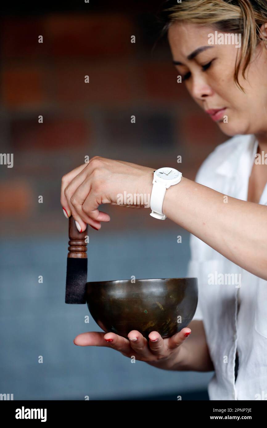 Woman using a tibetan singing bowl.  Self care, meditation, recreation, yoga and sound therapy.  Vietnam. Stock Photo