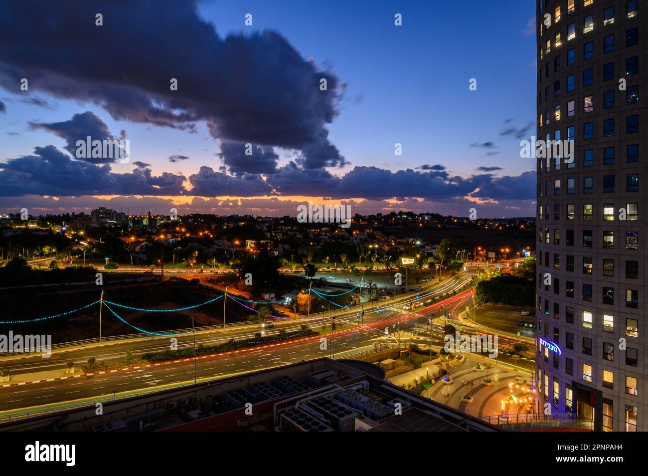 Blue Moment: A Street Illuminated by Streetlights, Overlooking Distant Sunset and Clouds from Above Stock Photo