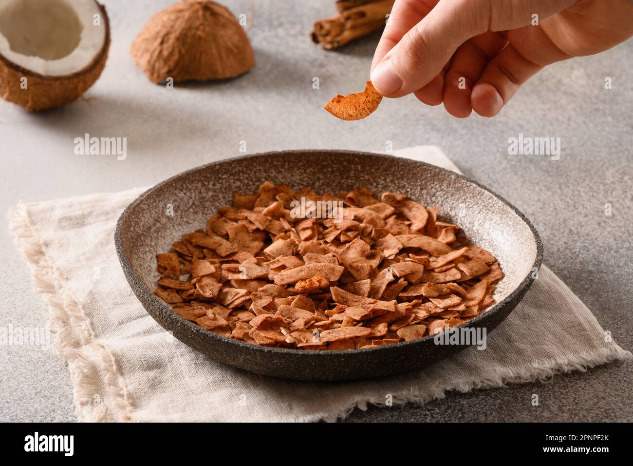 Coconut chips with cinnamon powder in child hand on gray background. Sri lankan vegan sugar free snack for children. Close up. Stock Photo