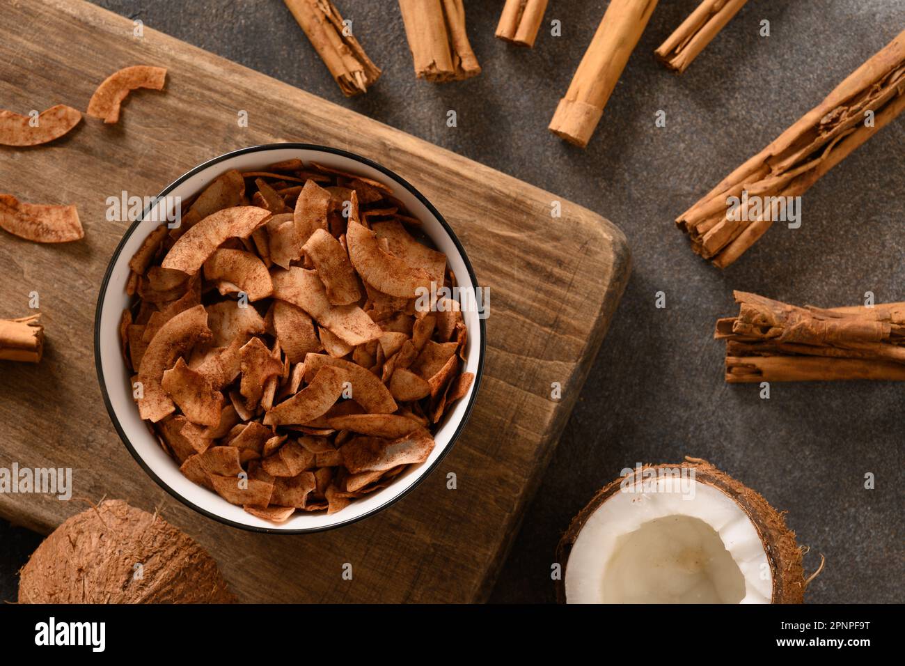 Coconut chips with cinnamon in bowl on brown background, home drying. Vegan and sugar free dessert. Top view. Sri lankan local snack. Stock Photo