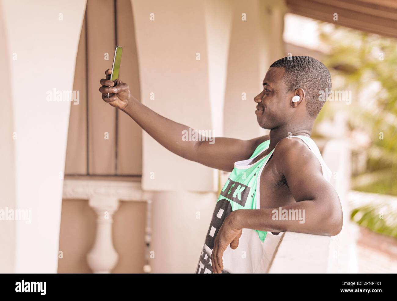 Young black male tourist takes a selfie on a hotel terrace while listening to music on true wireless earphones. Enjoying modern technology and capturi Stock Photo