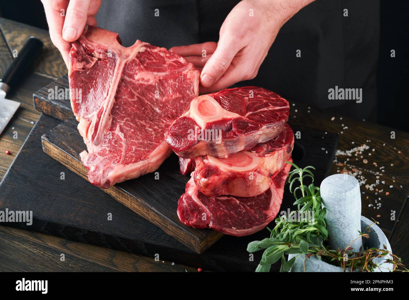 Steak beef meat. Chef cutting steak beef. Mans hands hold raw steak Tomahawk on rustic wooden cutting board on black background. Cooking, recipes and Stock Photo