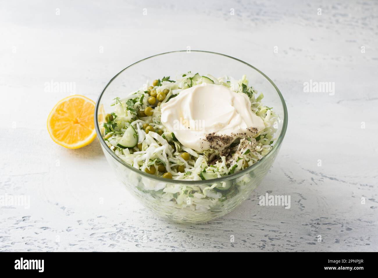 Glass bowl of cabbage salad with cucumbers, green peas, chopped herbs, mayonnaise dressing and lemon. Cooking delicious homemade salad. Step-by-step i Stock Photo