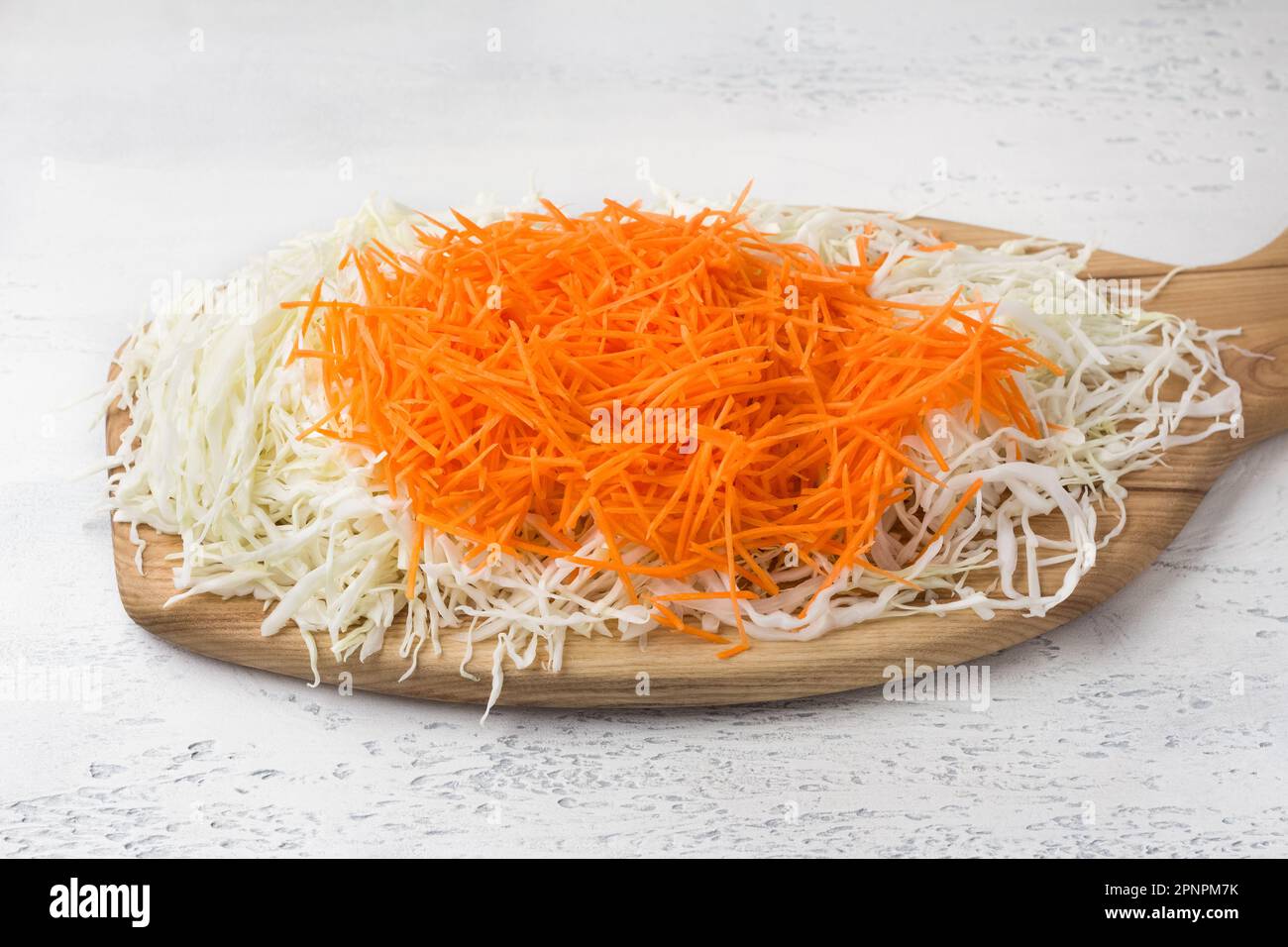 Wooden board with chopped cabbage and grated carrots on a light blue