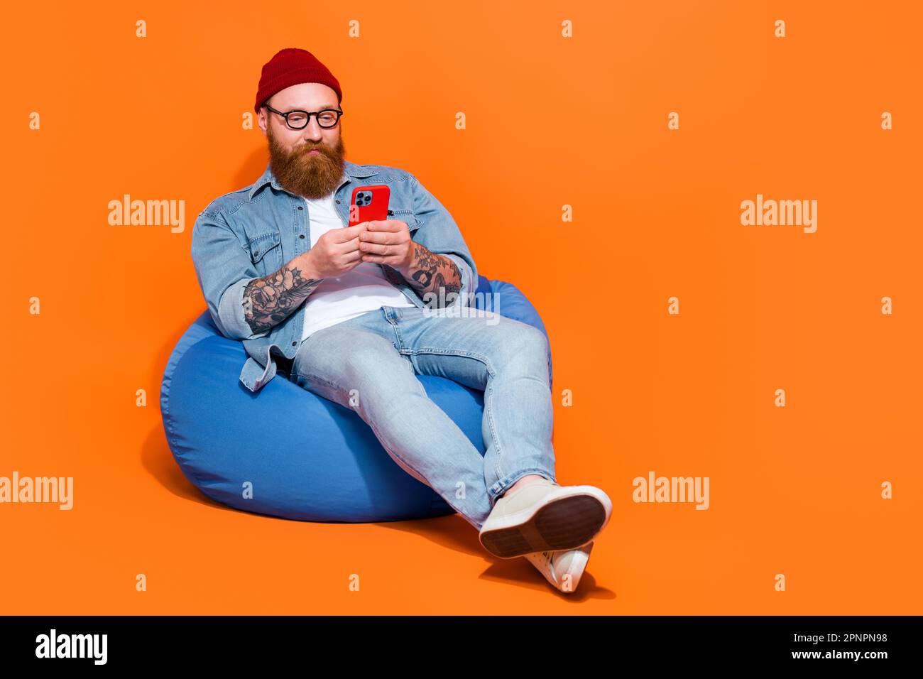 Photo of hipster brutal young guy sit bean chair use gadget watch youtube  videos isolated on bright color background Stock Photo - Alamy