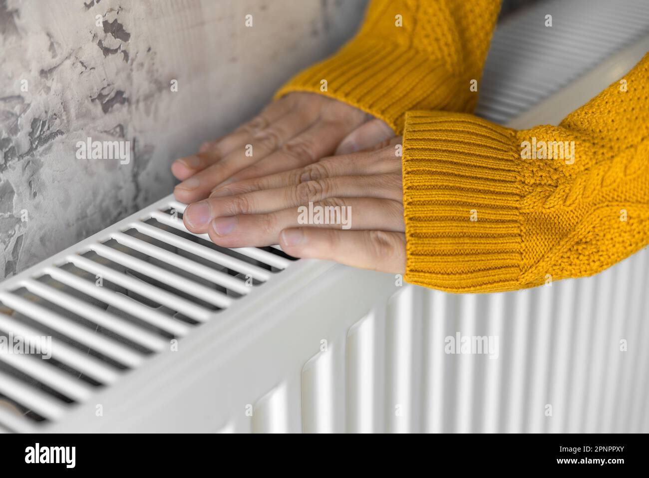 Closeup of man warming his hands in yellow sweater on the heater at home during cold winter days