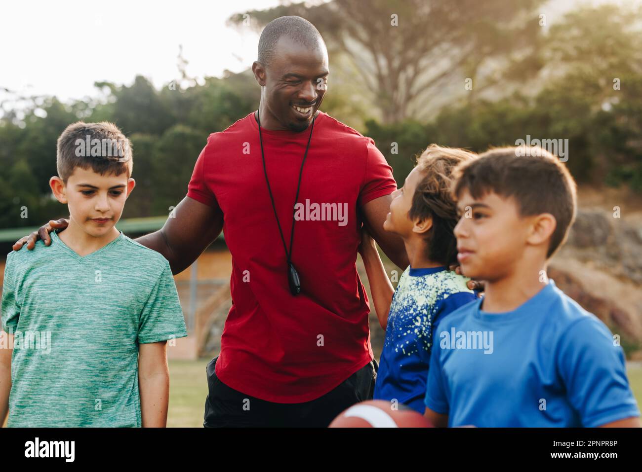 Happy coach standing with his elementary school rugby team. Sports instructor training a group of children in primary school. Student mentorship and d Stock Photo