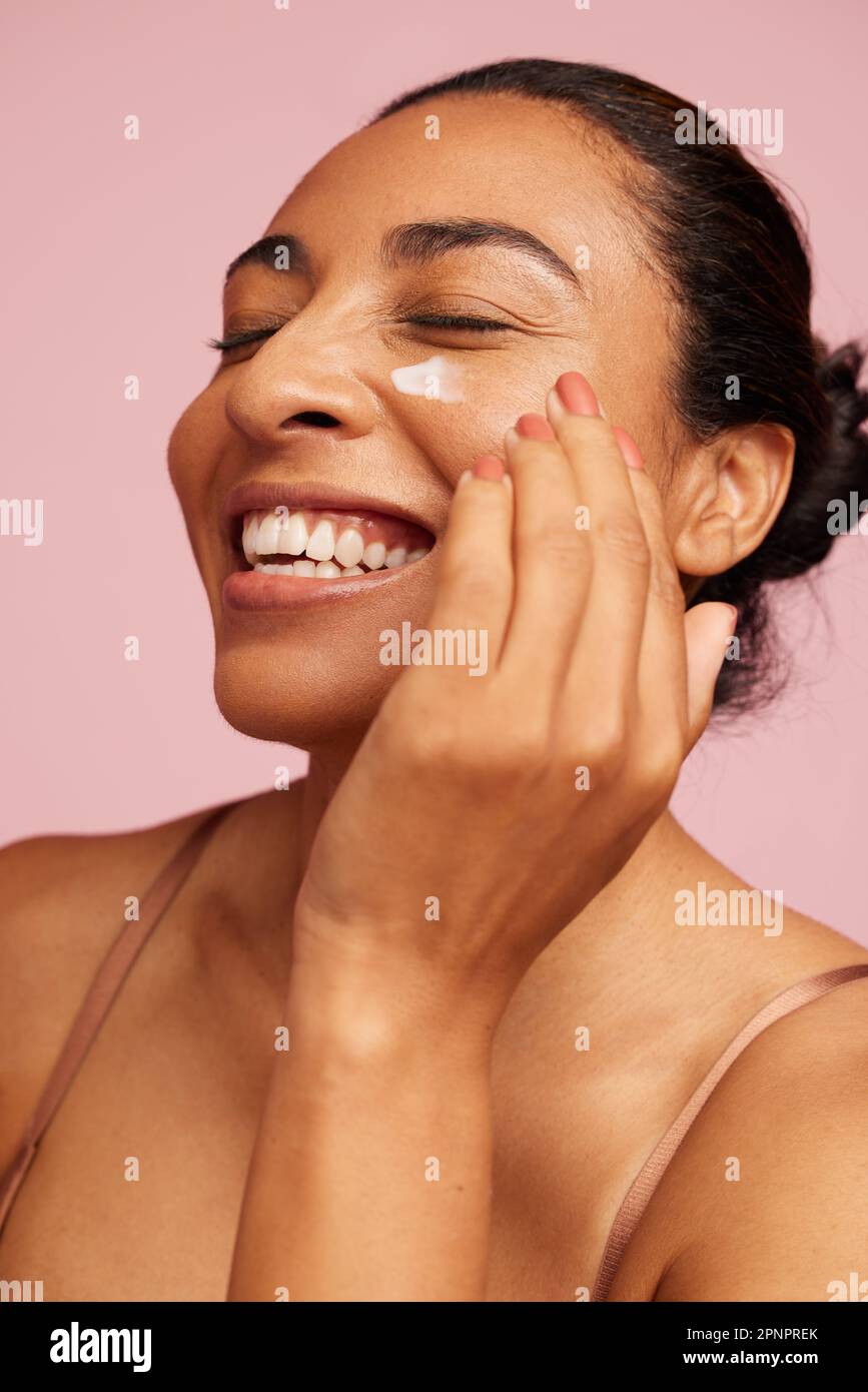 Close-up of a beautiful woman applying moisturizer cream on her face. Female using anti-aging cream and smiling. Stock Photo