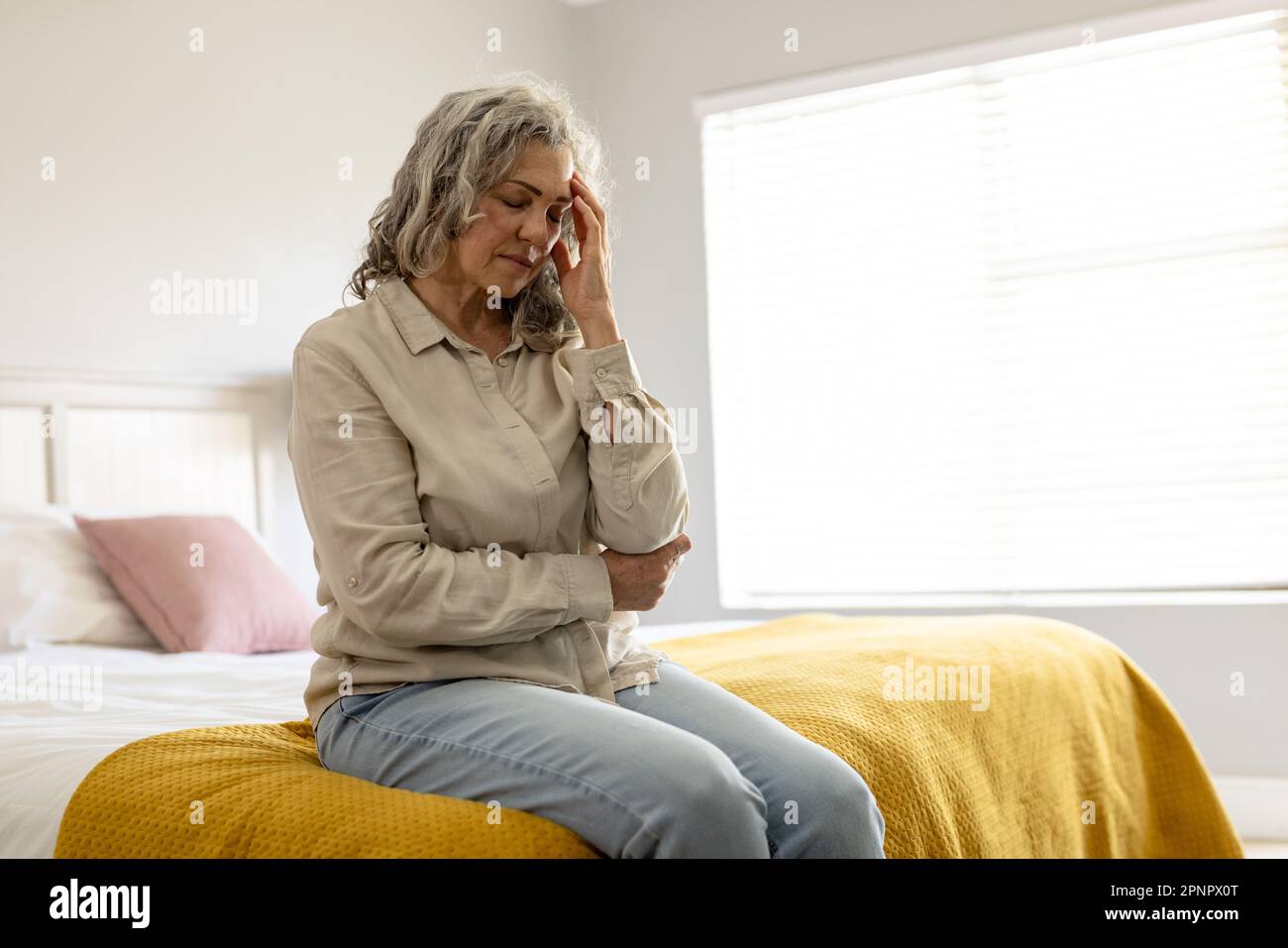 Worried senior caucasian woman sitting on bed holding her head Stock Photo