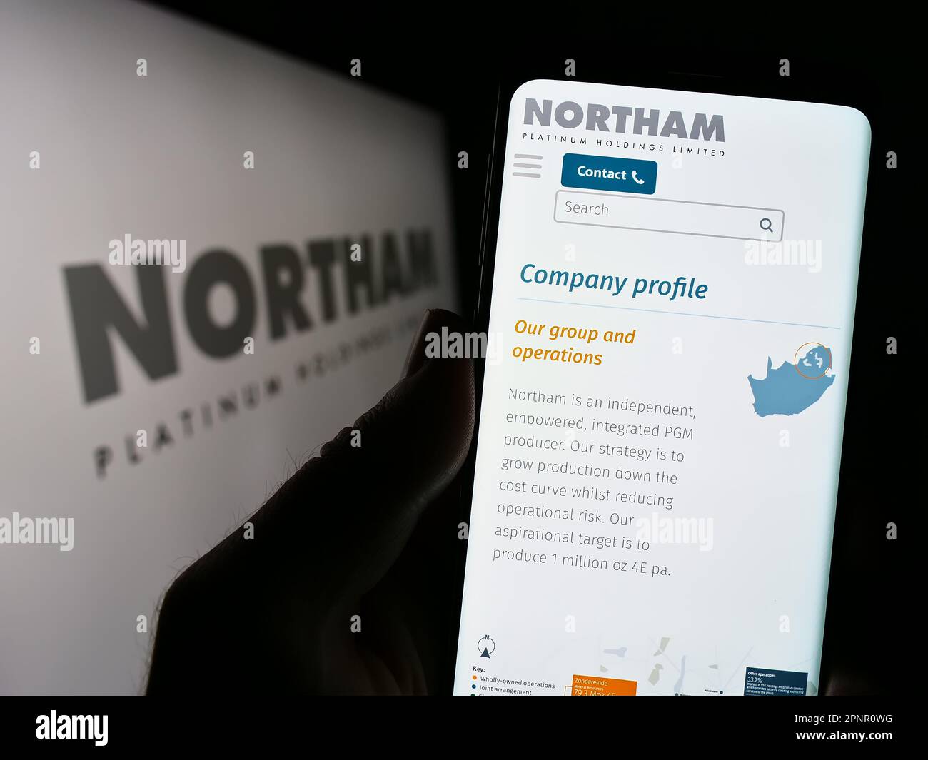 Person holding cellphone with website of company Northam Platinum Holdings Limited on screen in front of logo. Focus on center of phone display. Stock Photo