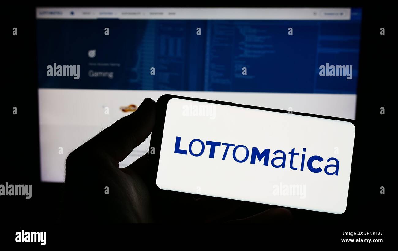 Person holding smartphone with logo of Italian gambling company Lottomatica S.p.A. on screen in front of website. Focus on phone display. Stock Photo