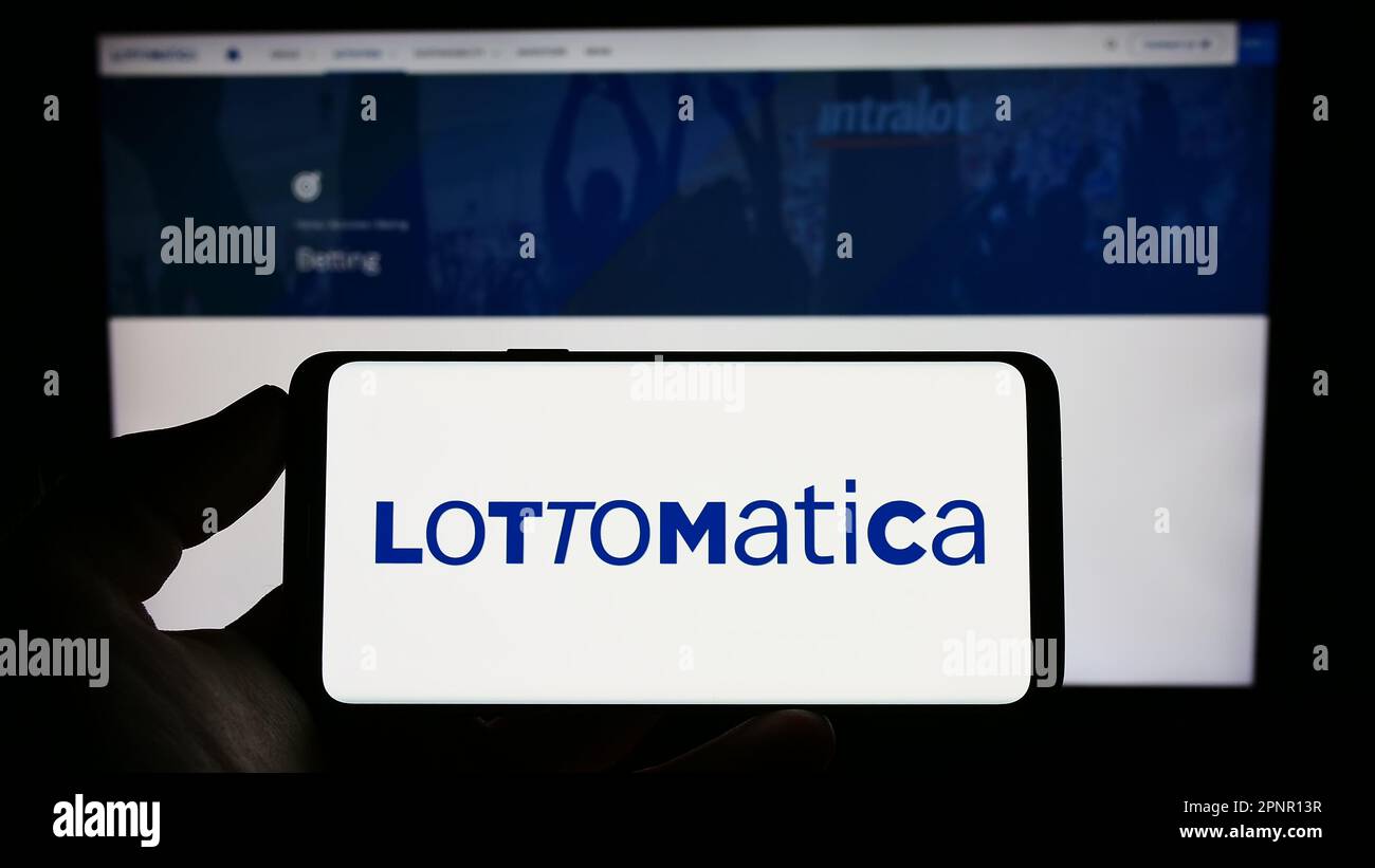 Person holding mobile phone with logo of Italian gambling company Lottomatica S.p.A. on screen in front of web page. Focus on phone display. Stock Photo