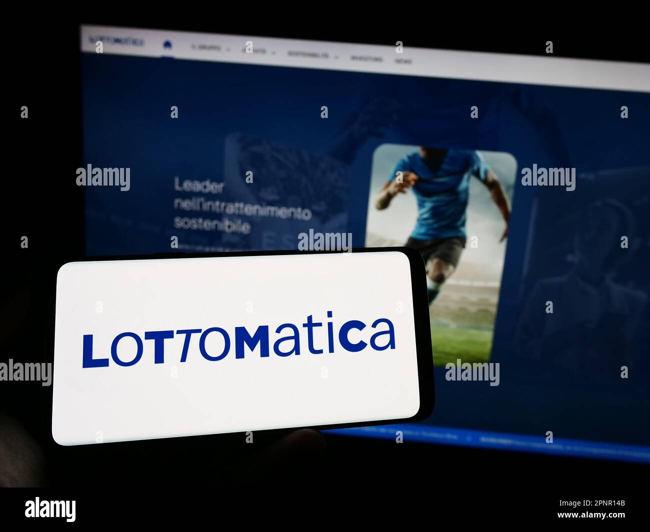 Person holding cellphone with logo of Italian gambling company Lottomatica SpA on screen in front of business webpage. Focus on phone display. Stock Photo