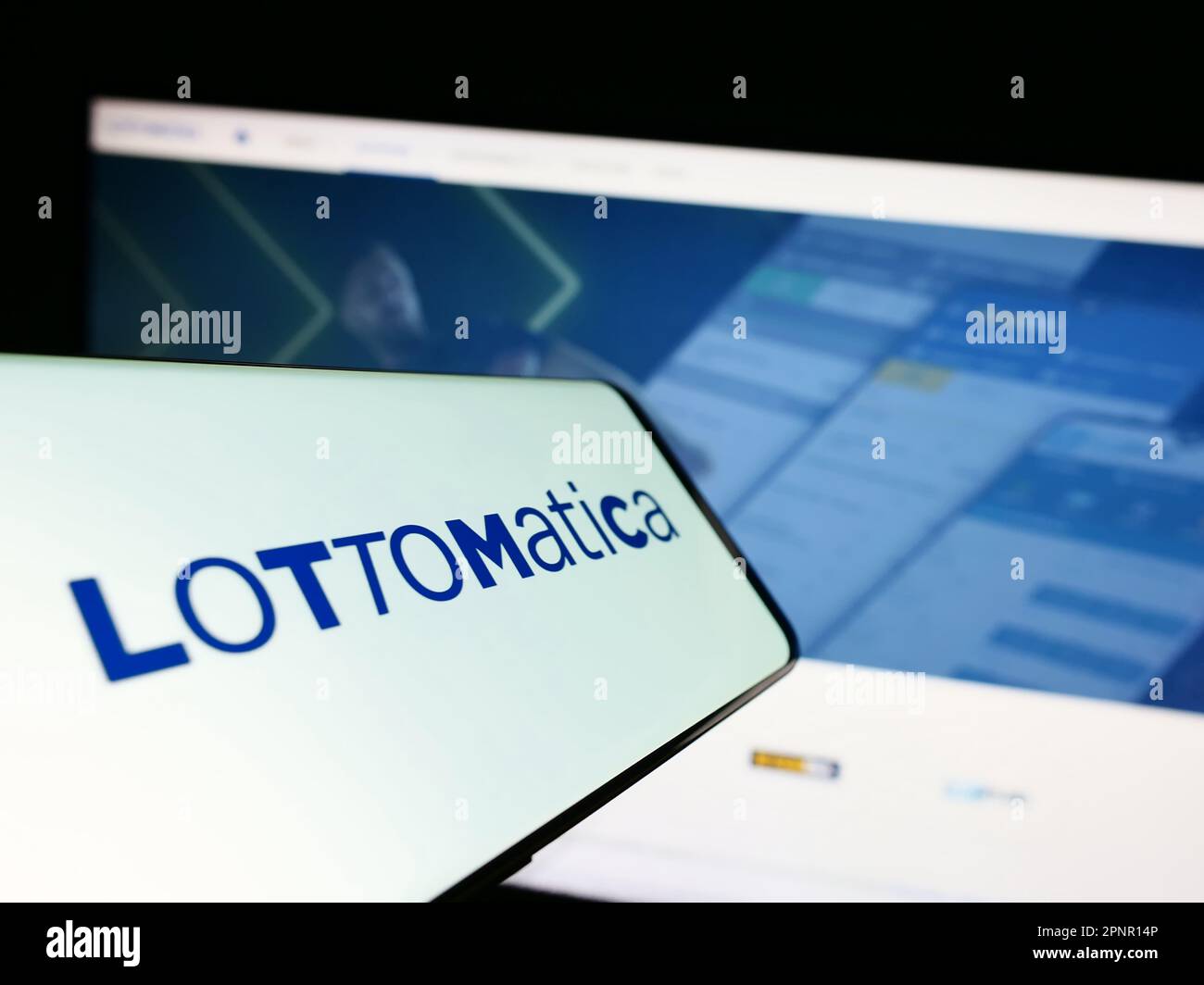 Cellphone with logo of Italian gambling company Lottomatica S.p.A. on screen in front of website. Focus on center-right of phone display. Stock Photo