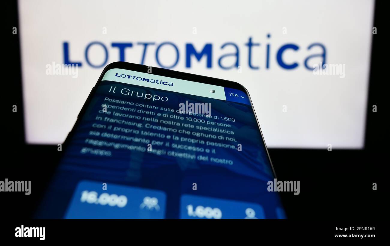 Mobile phone with webpage of Italian gambling company Lottomatica S.p.A. on screen in front of business logo. Focus on top-left of phone display. Stock Photo