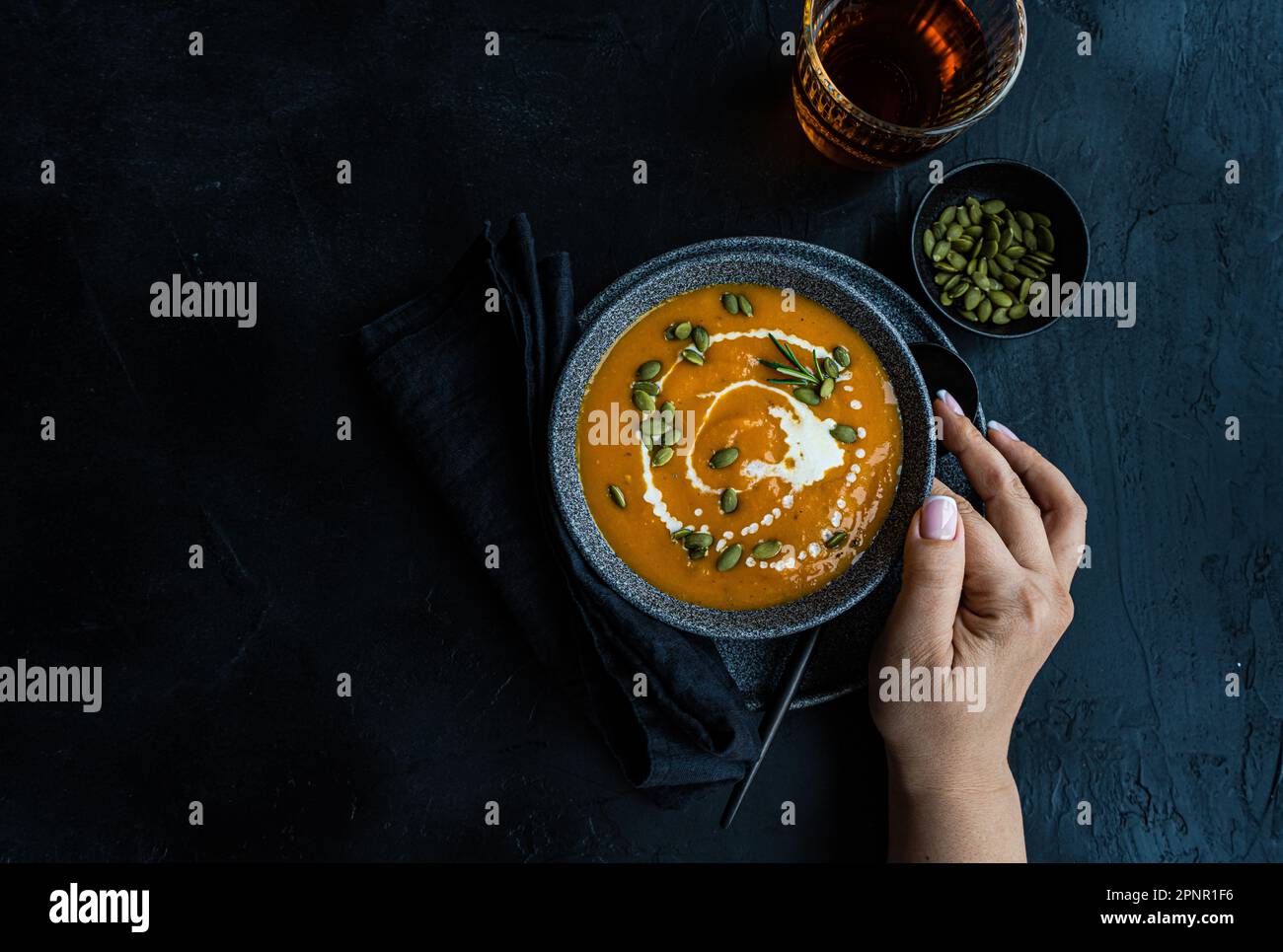 Overhead view of a woman reaching for a bowl of pumpkin soup with sour cream and a glass of wine Stock Photo