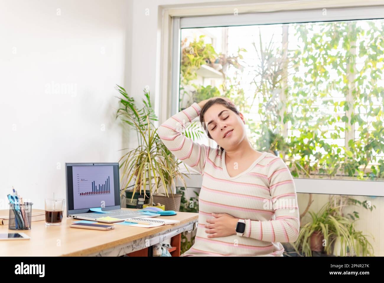 A woman stretching and exercising in an office setting, seeking relief from a sedentary position Stock Photo