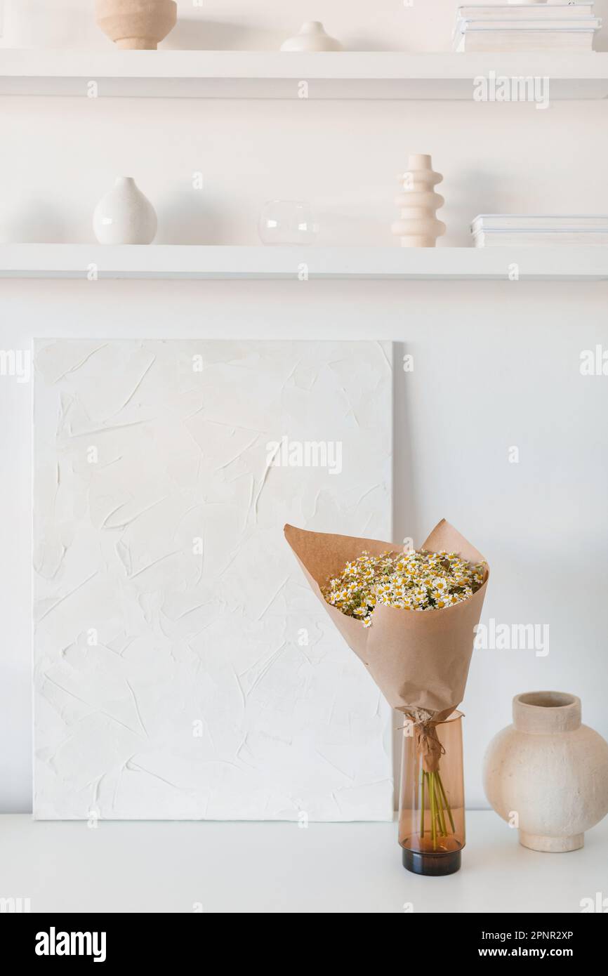 Bunch of flowers wrapped in brown paper in a vase by a shelving unit Stock Photo