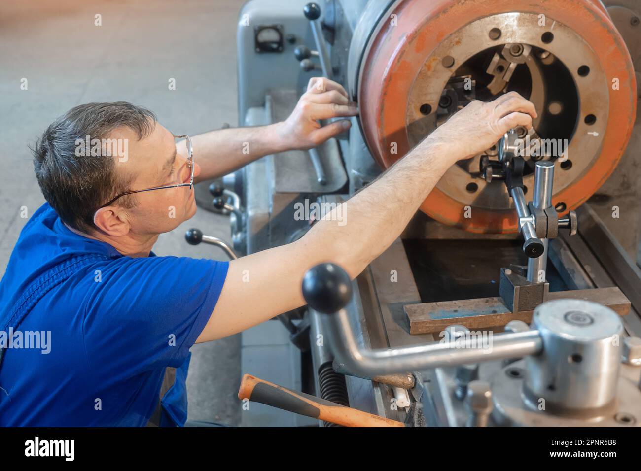 Turner with glasses working at lathe on shop floor. Turner aligns brake