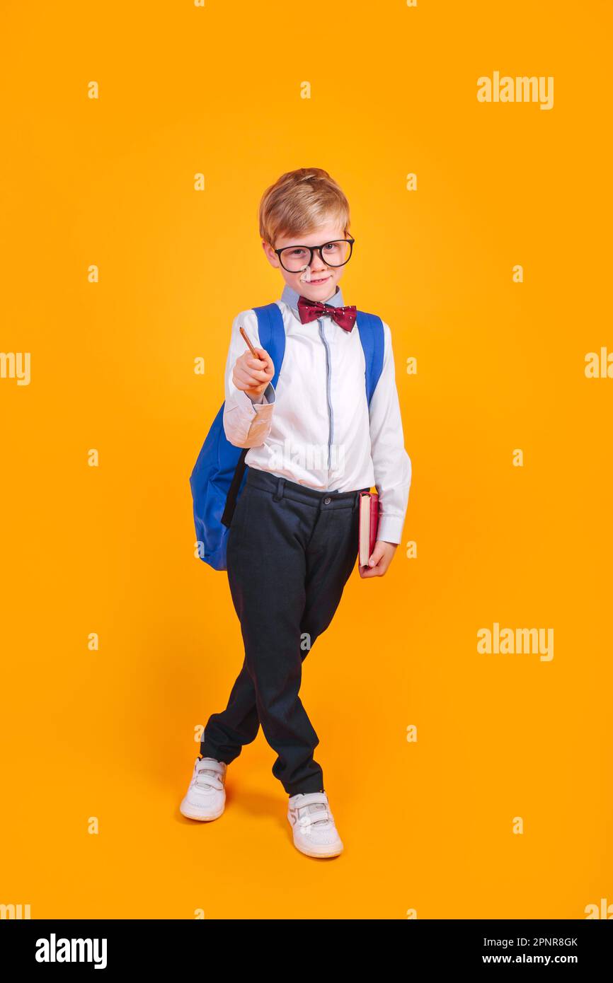 Little school boy in eyeglasses and bowtie with backpack holding books ...