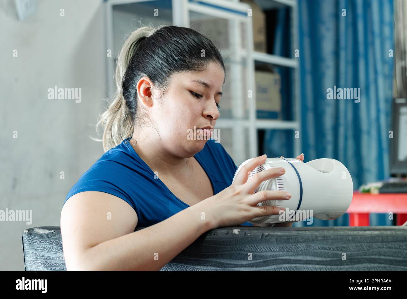 young latina woman trying to disassemble a mosquito-trapping fan, to see how it works Stock Photo
