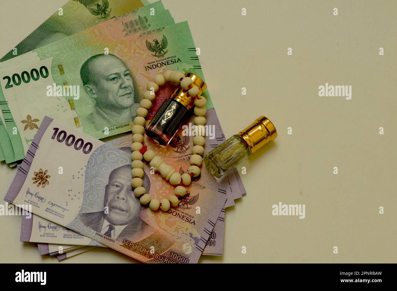 Close up of money, Indonesian rupiah banknote and perfume and prayer beads, in shallow focus Stock Photo