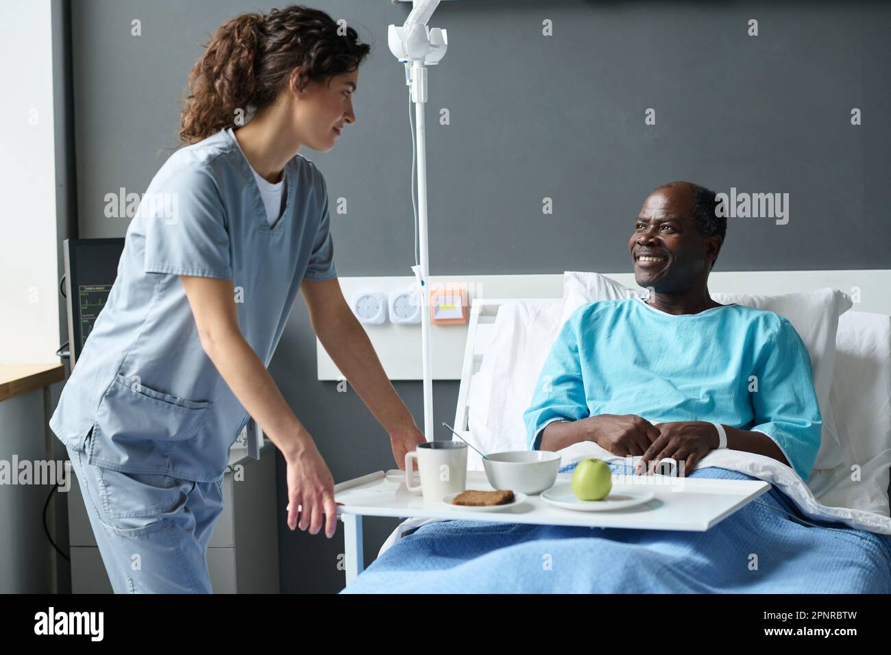 Young nurse in uniform bringing lunch for elderly patient while he