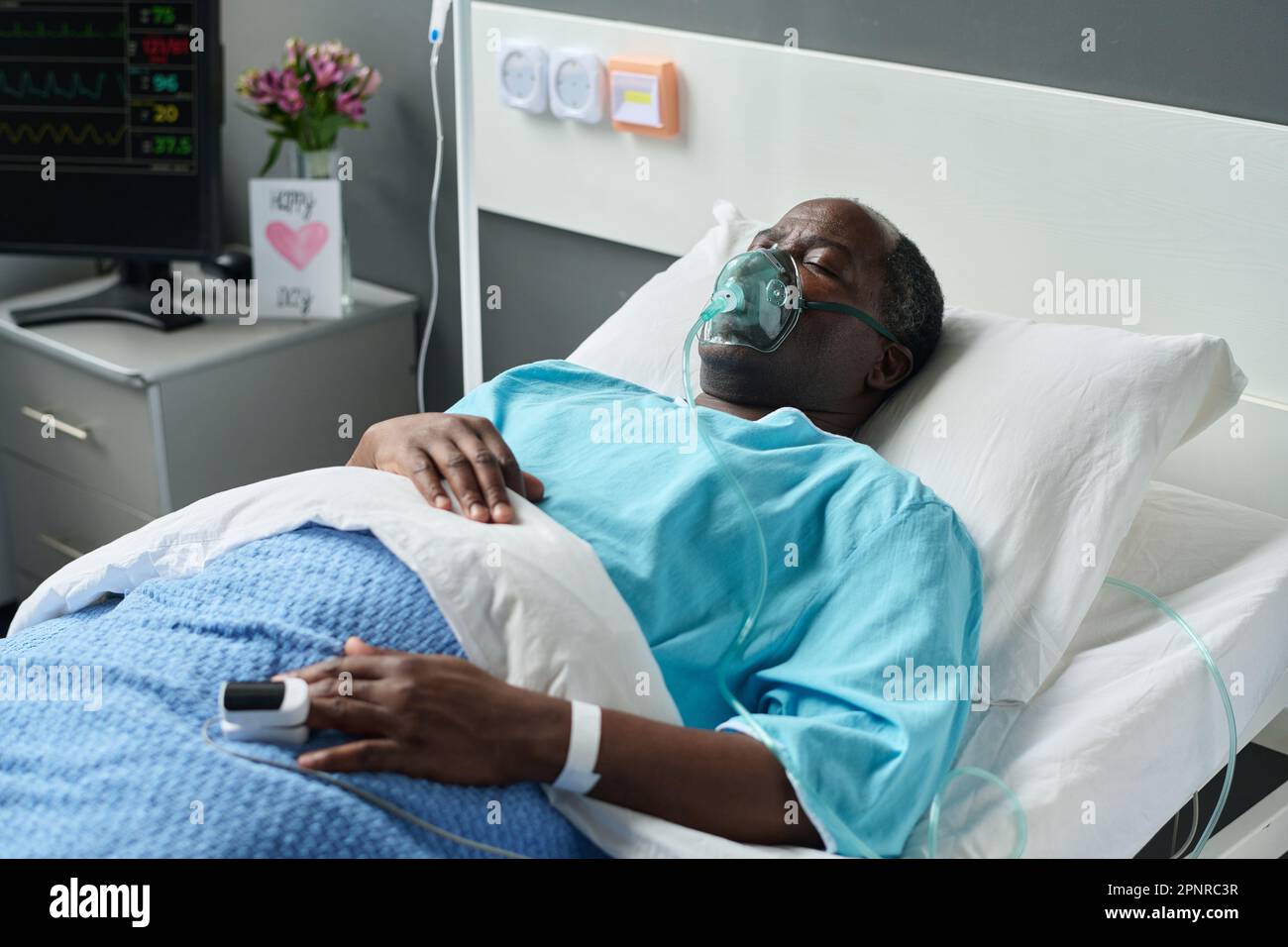 African American unconscious man in oxygen mask lying on bed in