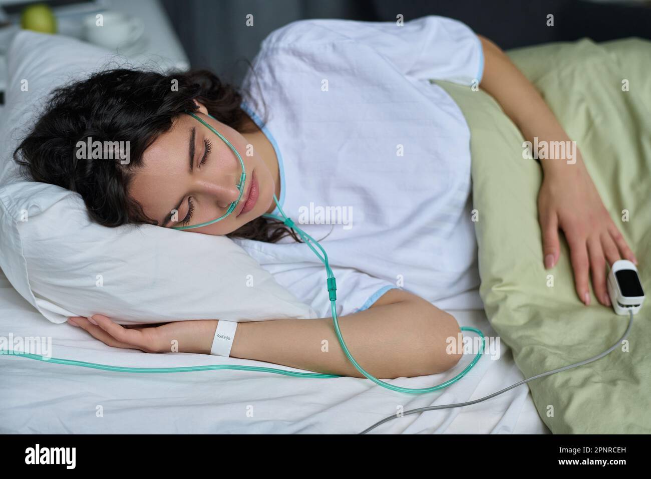 Young woman sleeping with oxygen tube on bed in hospital ward Stock