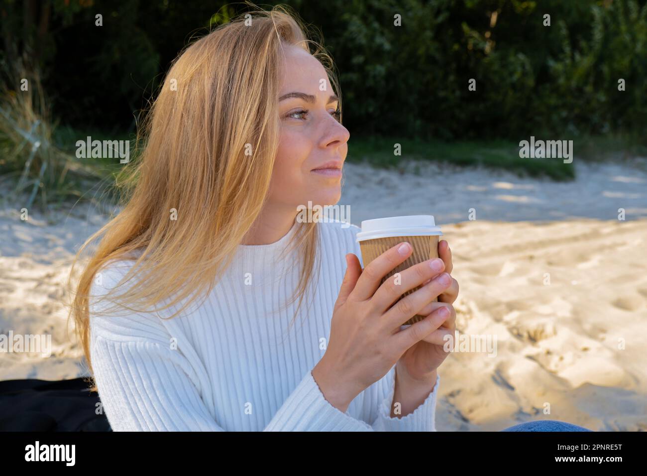 Happy young woman drinking coffee from paper cup takeaway on the beach ...