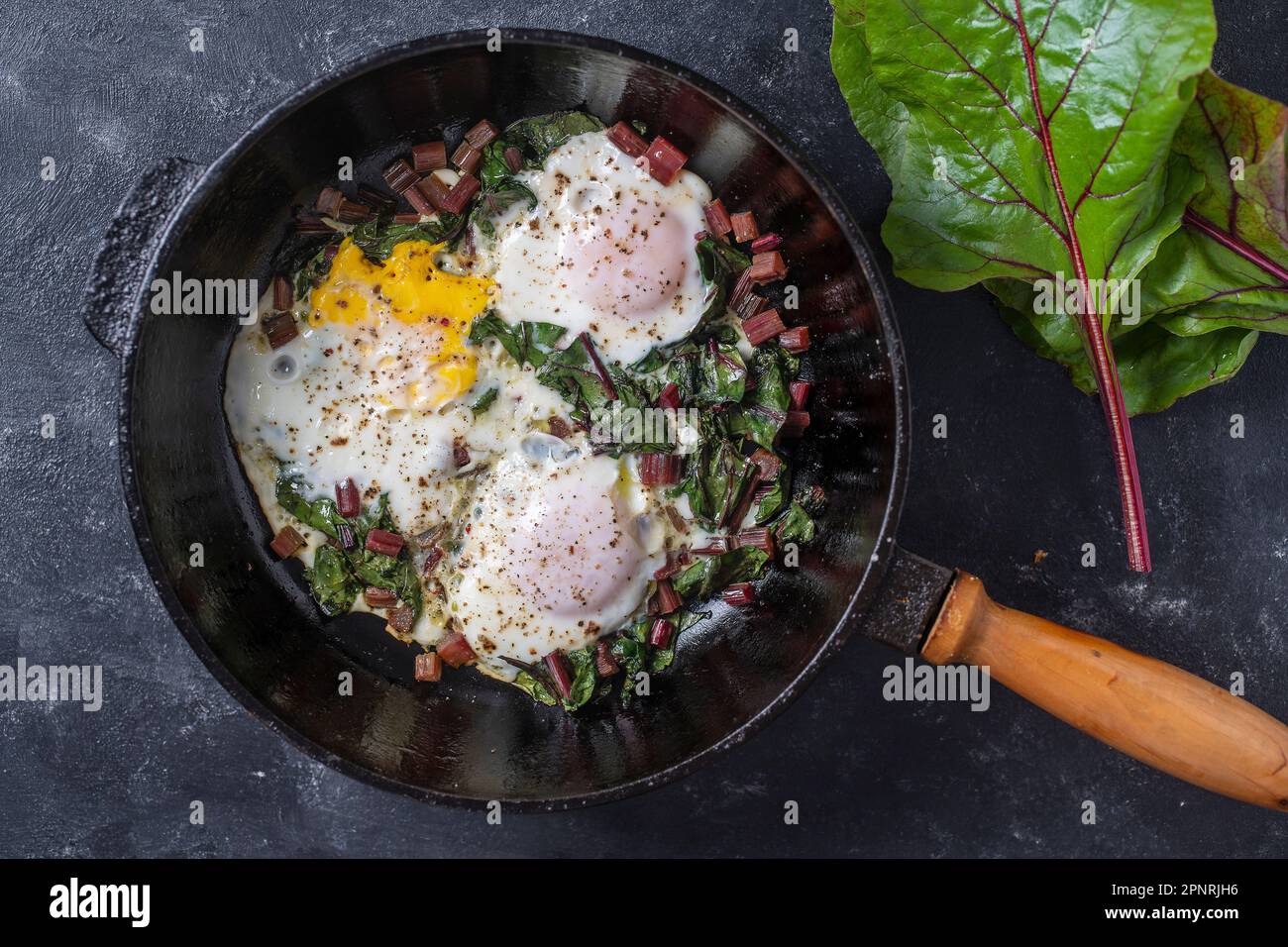 Fried eggs with green beet leaves, onion, pepper and spices in cast iron pan, close up, top view Stock Photo