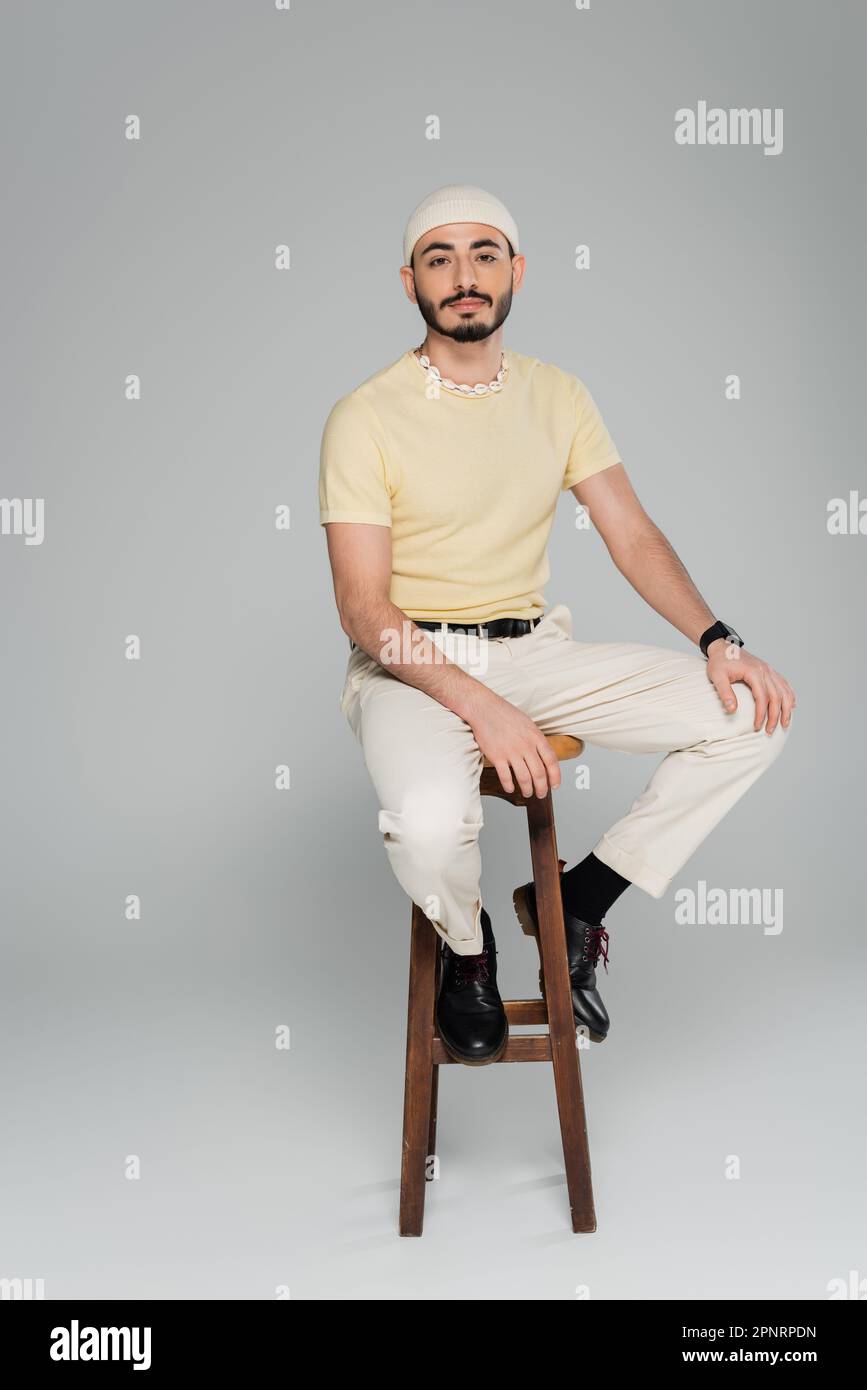 Full length of trendy homosexual man sitting on chair on grey background,stock image Stock Photo