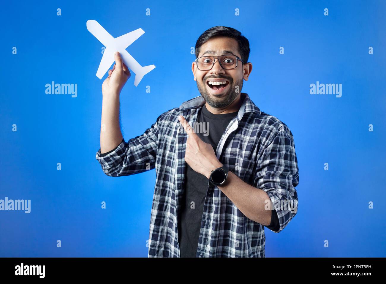 Toothy smile, travel destination, journey. One university student clutching paper cut airplane and pointing. Stock Photo