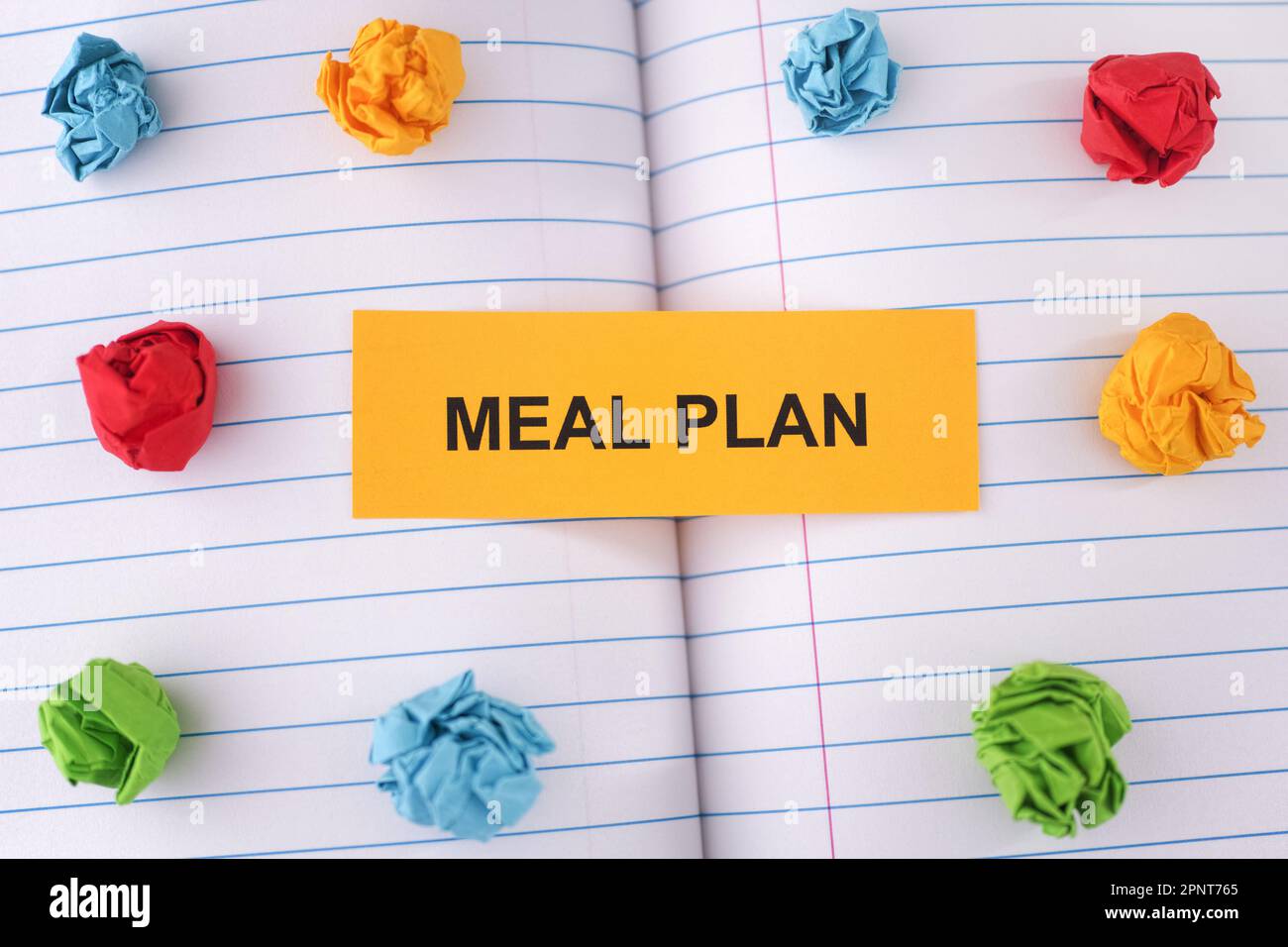 A paper note with the words Meal Plan on notebook sheet with some colorful crumpled paper balls around it. Close up. Stock Photo