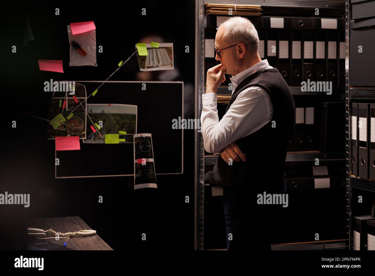Senior officer working overtime at mysterious criminal case, analyzing files with scene crime evidence, checking victim report. Private detective discovery potential suspect in arhive room Stock Photo