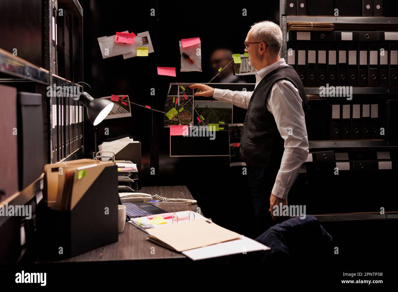 Elderly private detective checking federal investigation files, working overtime at criminal case in arhive room. Senior police officer analyzing crime scene evidence, looking at suspect report Stock Photo