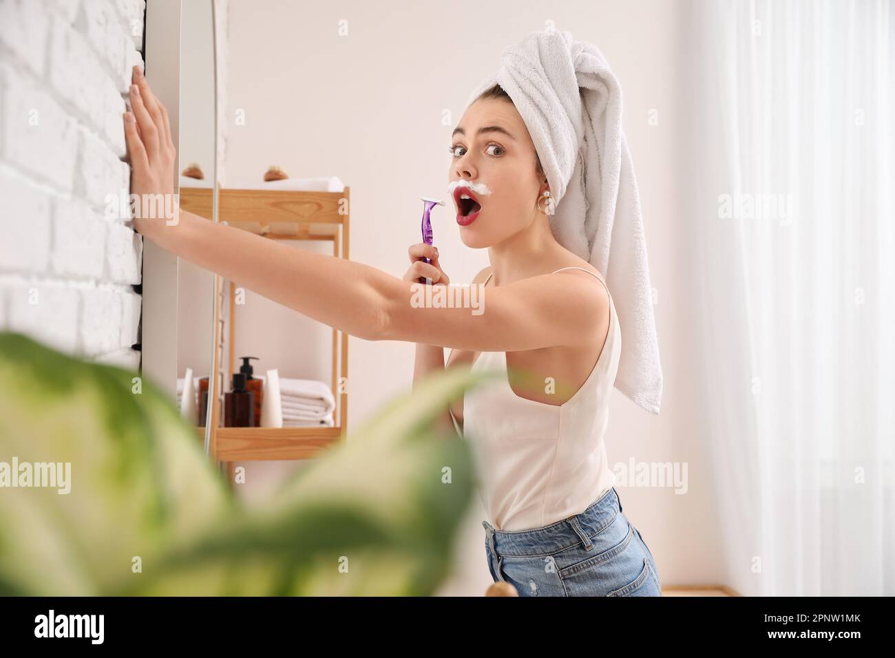Young woman shaving face with razor near mirror in bathroom Stock Photo