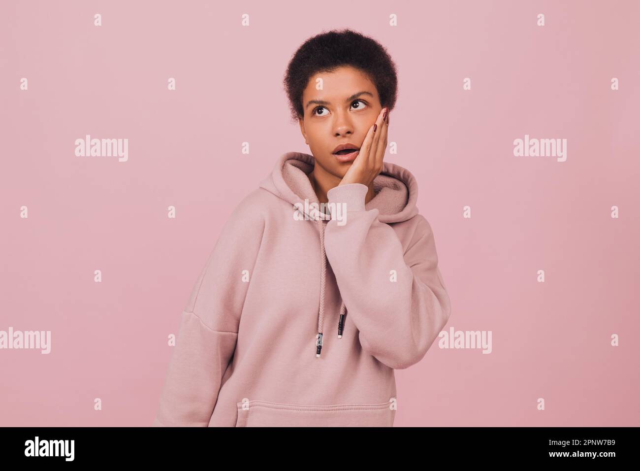Excited black girl standing on pink backdrop. Young woman wearing casual clothes standing with shocked face emotion and looking up Stock Photo