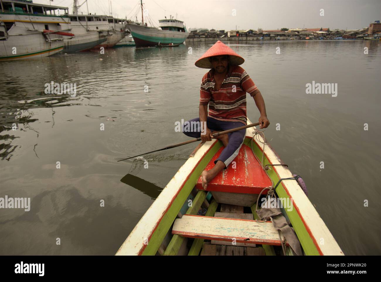 A man is steering a boat hired for coastal transportation, on coastal water at the traditional Sunda Kelapa Port in Penjaringan, North Jakarta, Jakarta, Indonesia. Stock Photo
