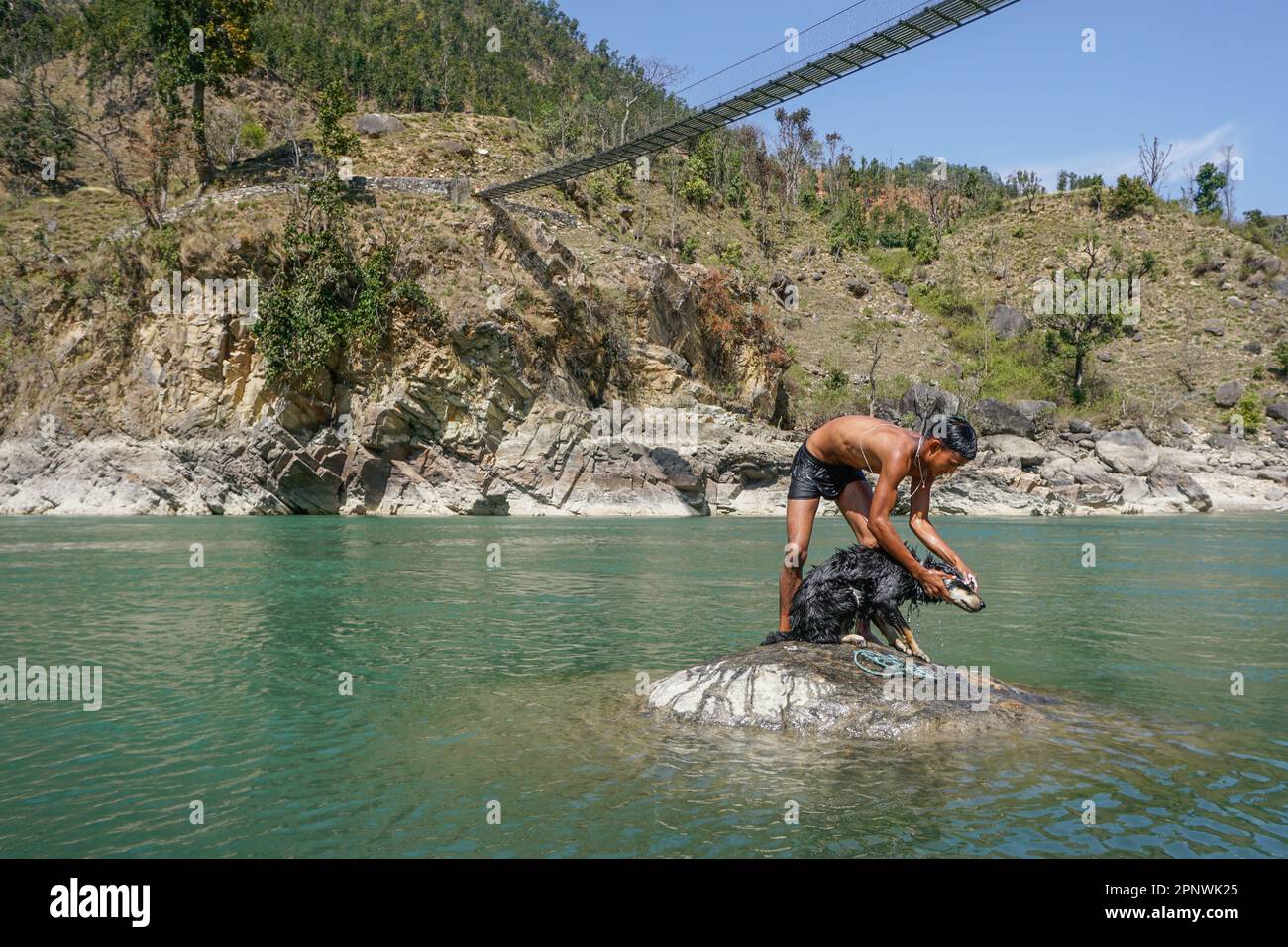 Hasta Bahadur Shahi, 18, bathes his dog, Johny, in Karnali River in Dailekh, Nepal on March 11, 2022. He enjoys spending time with 1-year-old Johny in the river on Saturdays during school holidays. (Shilu Manandhar/Global Press Journal) Stock Photo
