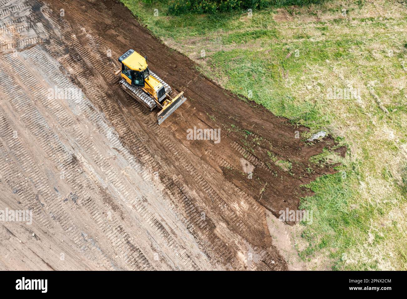 yellow tracked bulldozer performs earthworks on construction site. aerial view from flying drone. Stock Photo