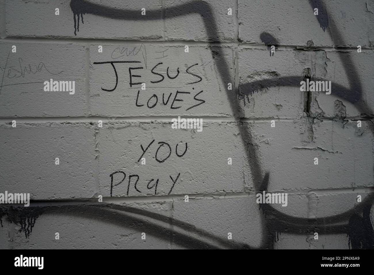 Jesus Loves You Pray sharpie writing on a painted brick wall Stock