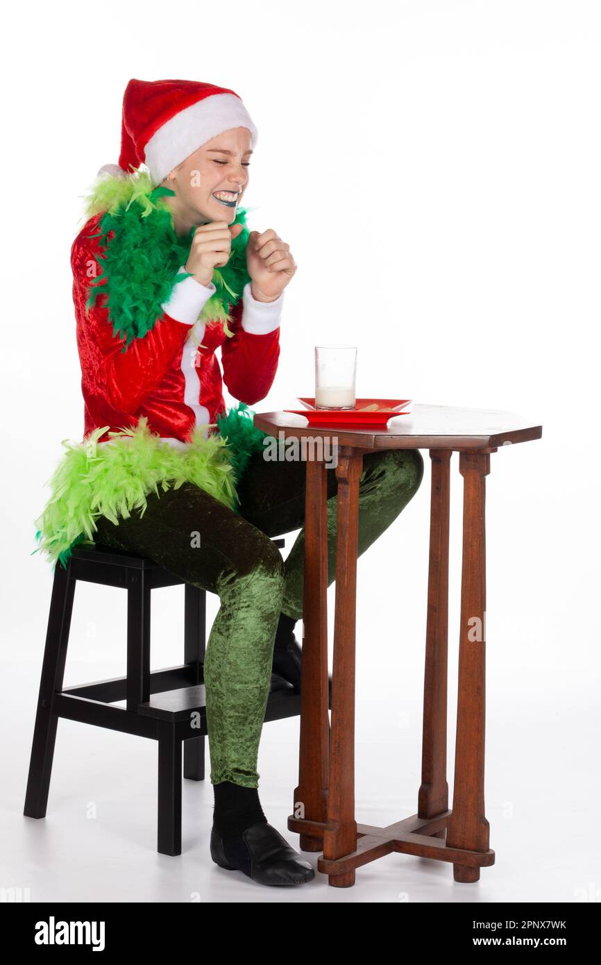 Full portrait of young girl wearing red santa clause hat like grinch with gleeful expression for milk and biscuits, isolated on white background. Glee Stock Photo