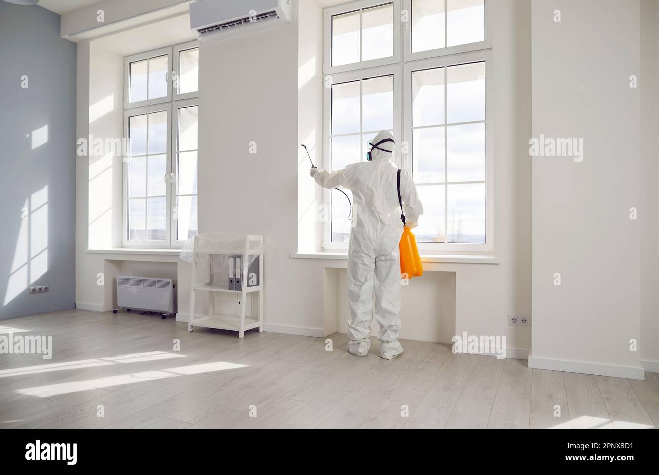 Pest control exterminator in protective suit spraying insecticide over windows in the house Stock Photo